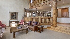 A spacious living area with a high ceiling, a wooden staircase, and a large window.