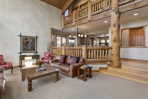 Un vaste salon comprenant un canapé en cuir marron, une table basse en bois et un fauteuil rouge. Un escalier en bois mène à un niveau supérieur doté d’un balcon.