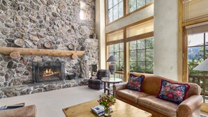 A stone fireplace, a leather sofa with floral cushions, and a coffee table with books and flowers.