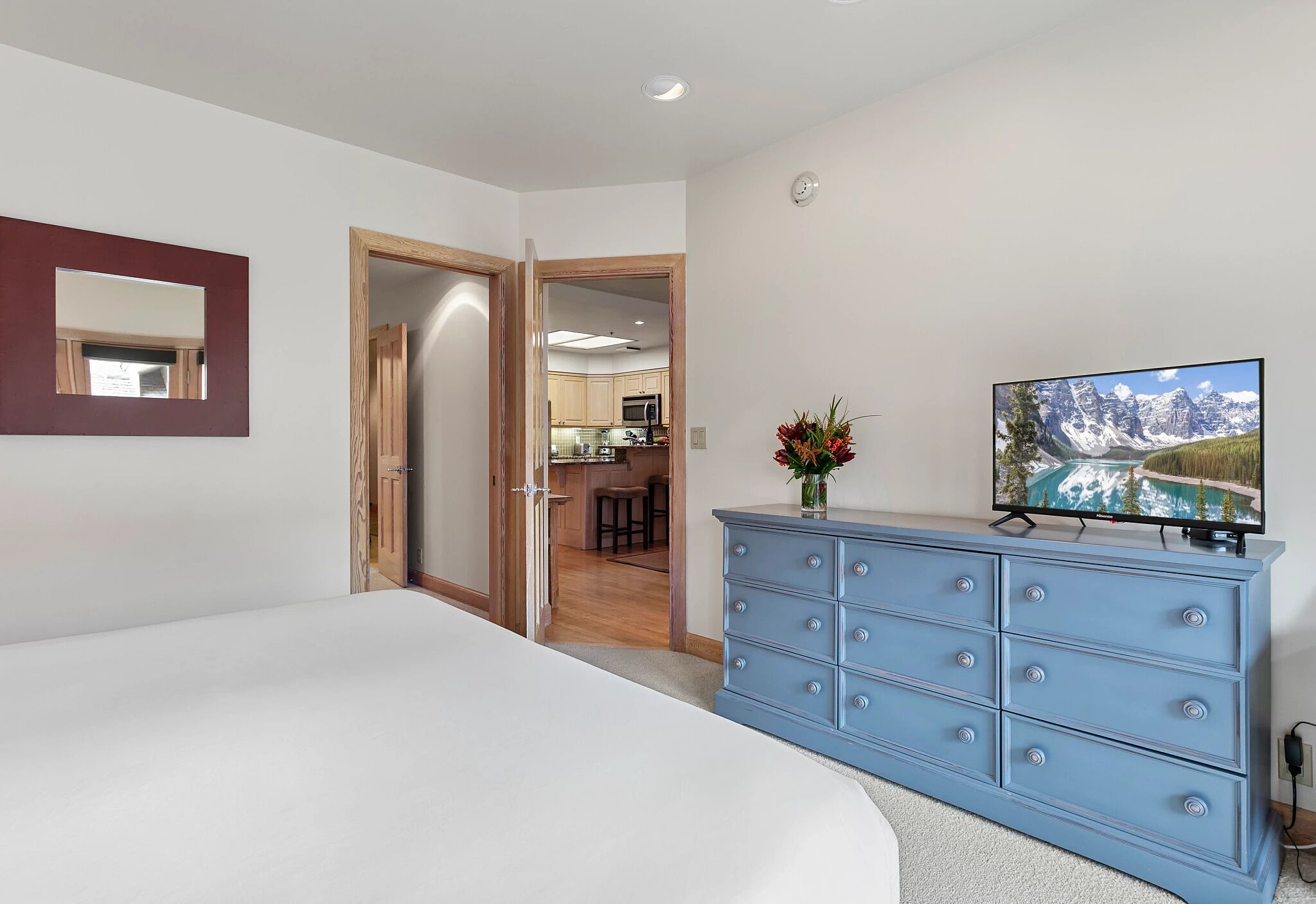 A bedroom with a large bed, a blue dresser, a TV, and a mirror on the wall.