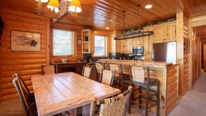 A log cabin interior with a wooden dining table, chairs, a kitchen area with a refrigerator, and a chandelier. - Comstock Lodge at Deer Valley Resort - Two Bedroom Condo with Hot Tub #101 2 Condo (Park City)