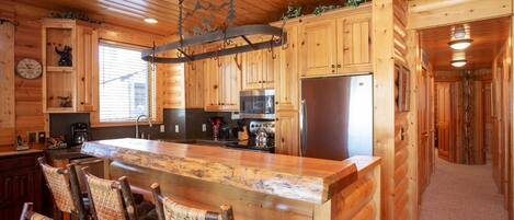 Cocina de cabaña de madera con una isla central, armarios de madera y una lámpara colgante.