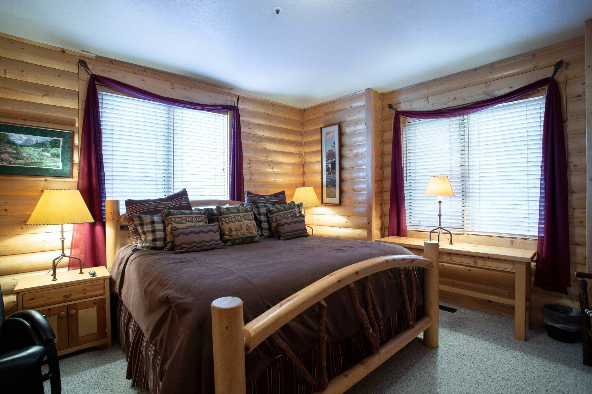 Ein gemütliches Schlafzimmer in einer Blockhütte mit einem großen Bett, zwei Nachttischen mit Lampen und einem Holztisch.
