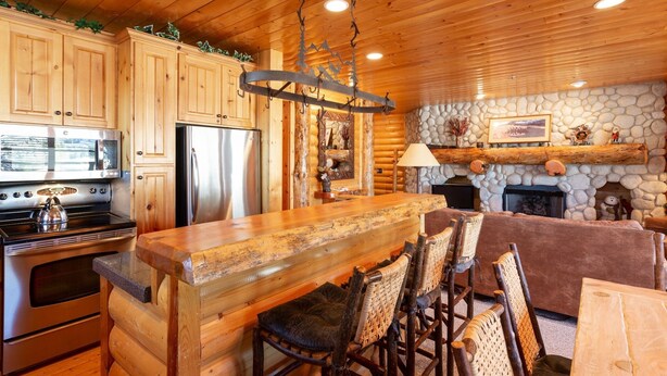 A log cabin interior with wooden cabinets, a central island bar, stone fireplace, and rustic decor. - Comstock Lodge at Deer Valley Resort - Two Bedroom Condo with Hot Tub #101 2 Condo (Park City)