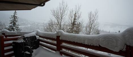 A snow-covered bench and railing, with a view of a snowy landscape and trees in the background.