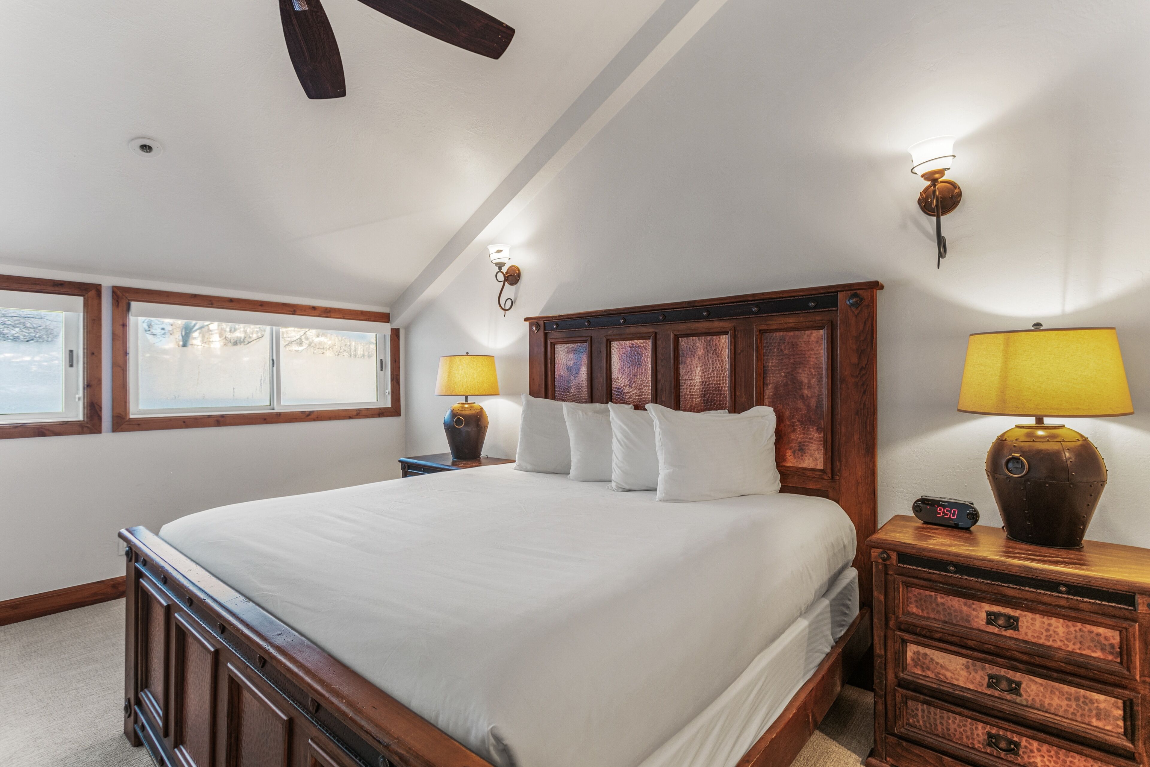 A bedroom with a large bed, two bedside lamps, a nightstand, and a clock.