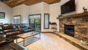 A modern living room with a stone fireplace, leather sofa, and a flat-screen TV mounted above the fireplace. - Lakeside at Deer Valley Resort - Two Bedroom Condo #1679 2 Condo (Park City)