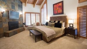 A bedroom with a stone fireplace, a bed with multiple pillows, a bench, a TV, and a nightstand. - Pinnacle at Deer Valley Resort - Four Bedroom Condo with Hot Tub #1065 4 Condo (Park City)