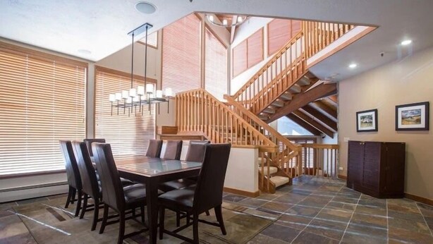 A dining area with a large table and chairs, a staircase, and a view of the outdoors. - Pinnacle at Deer Valley Resort - Four Bedroom Condo with Hot Tub #1065 4 Condo (Park City)