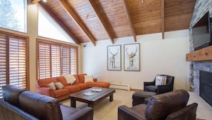 A spacious living room with a high ceiling, wooden beams, a fireplace, and large windows with blinds. - Pinnacle at Deer Valley Resort - Four Bedroom Condo with Hot Tub #1065 4 Condo (Park City)