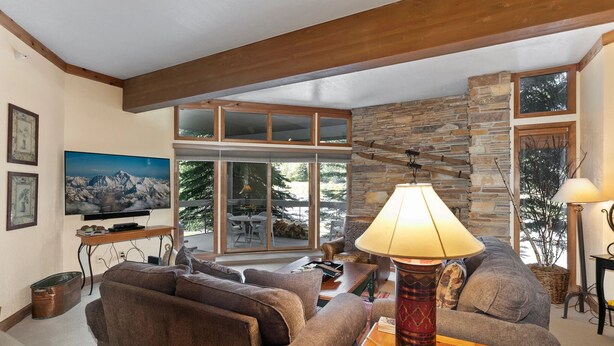 A cozy living room with a stone accent wall, large windows, and a comfortable sofa. - Powder Run at Deer Valley Resort - Two Bedroom Condo with Hot Tub #A13 2 Condo (Park City)