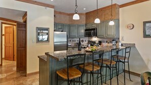 A kitchen with a central island, bar stools, a refrigerator, and a microwave. - Powder Run at Deer Valley Resort - Two Bedroom Condo with Hot Tub #A13 2 Condo (Park City)
