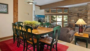 A dining area with a wooden table and chairs, a red rug, and a stone wall with a fireplace. - Powder Run at Deer Valley Resort - Two Bedroom Condo with Hot Tub #A13 2 Condo (Park City)