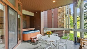 A covered outdoor area with a hot tub, white plastic chairs, and a table with flowers. - Powder Run at Deer Valley Resort - Two Bedroom Condo with Hot Tub #A13 2 Condo (Park City)
