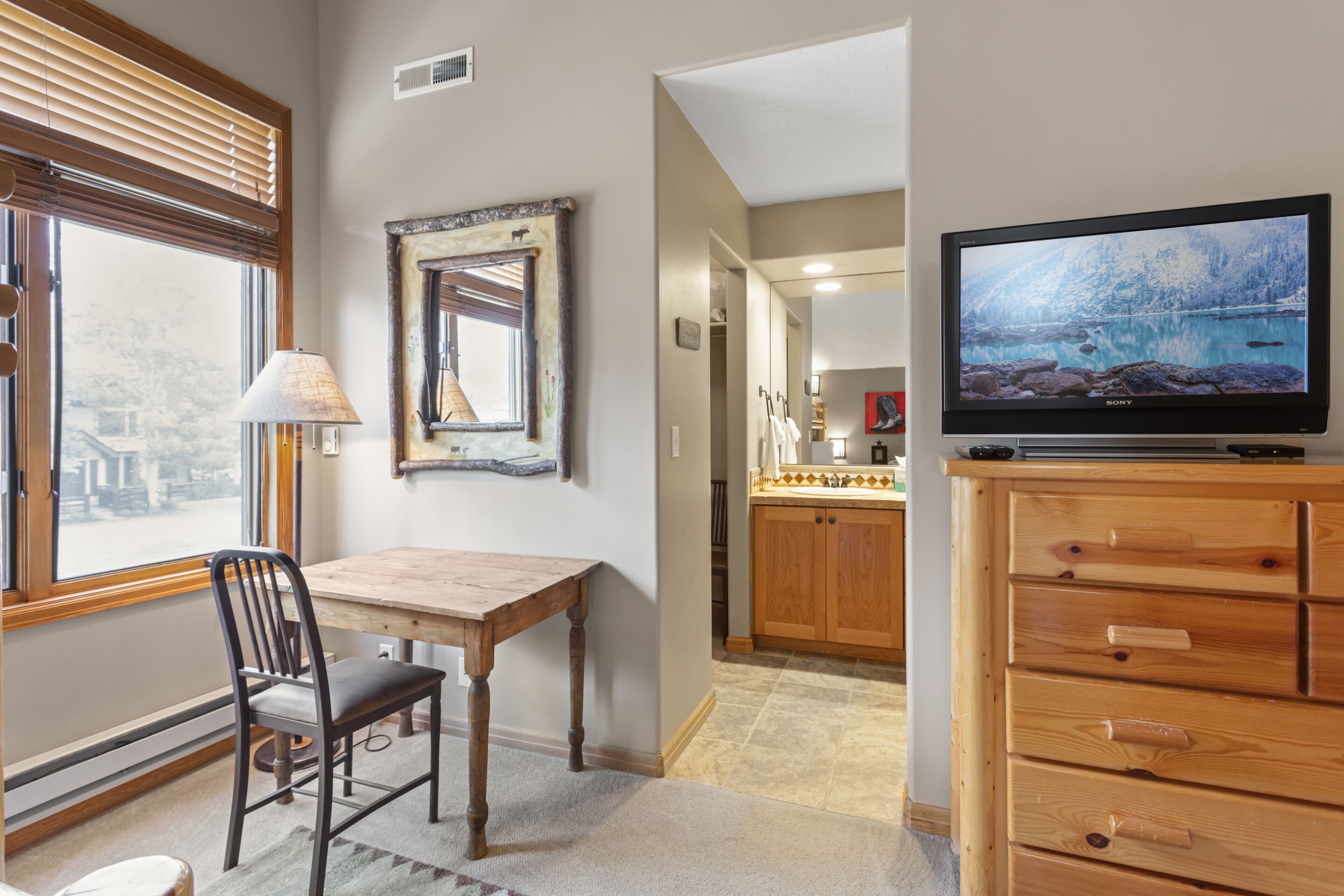 Una habitación con una mesa de comedor de madera, una silla, un televisor sobre un mueble de madera y una ventana con persianas.