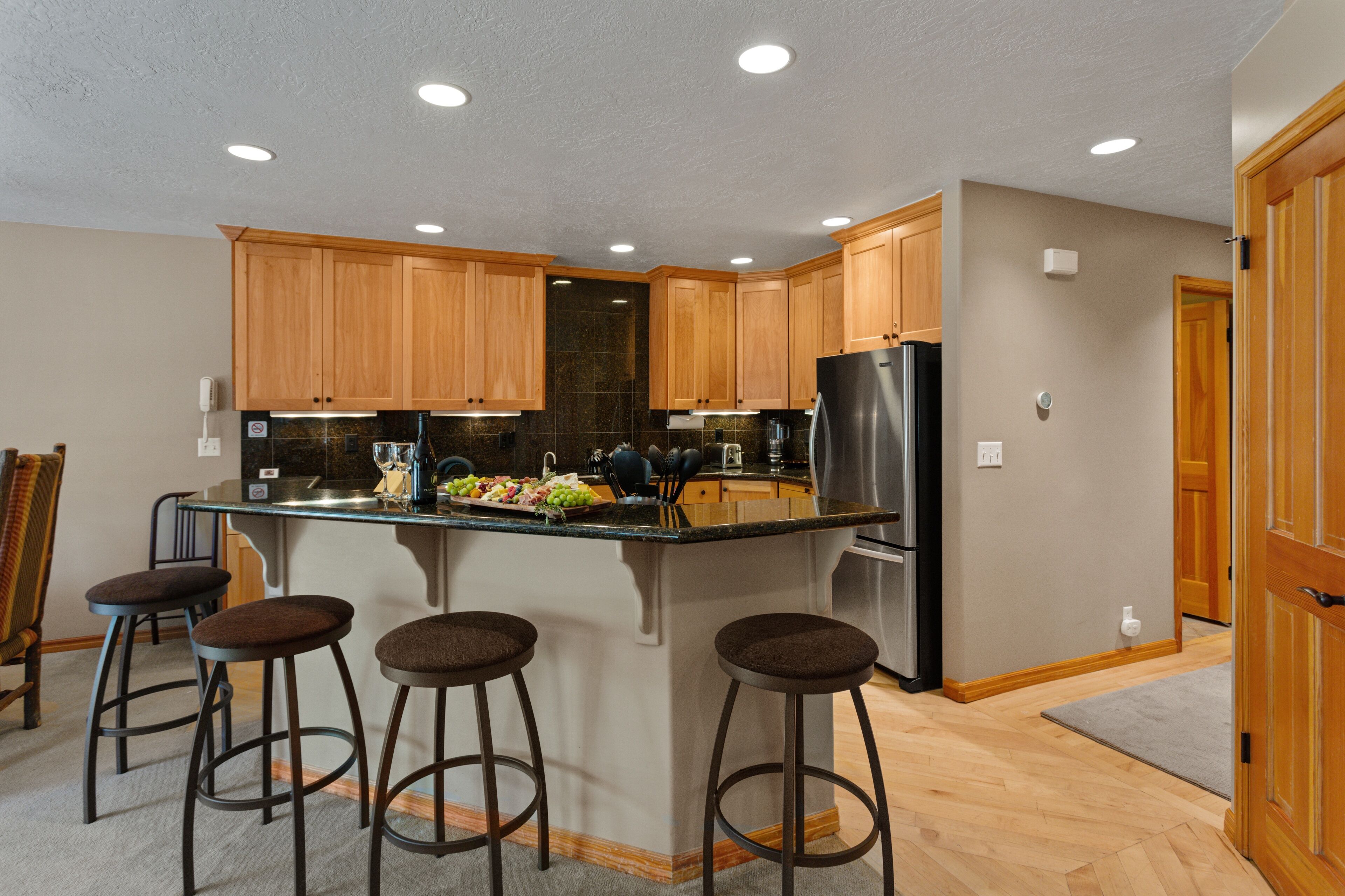 Una cocina moderna con armarios de madera, una isla central con taburetes y electrodomésticos de acero inoxidable.