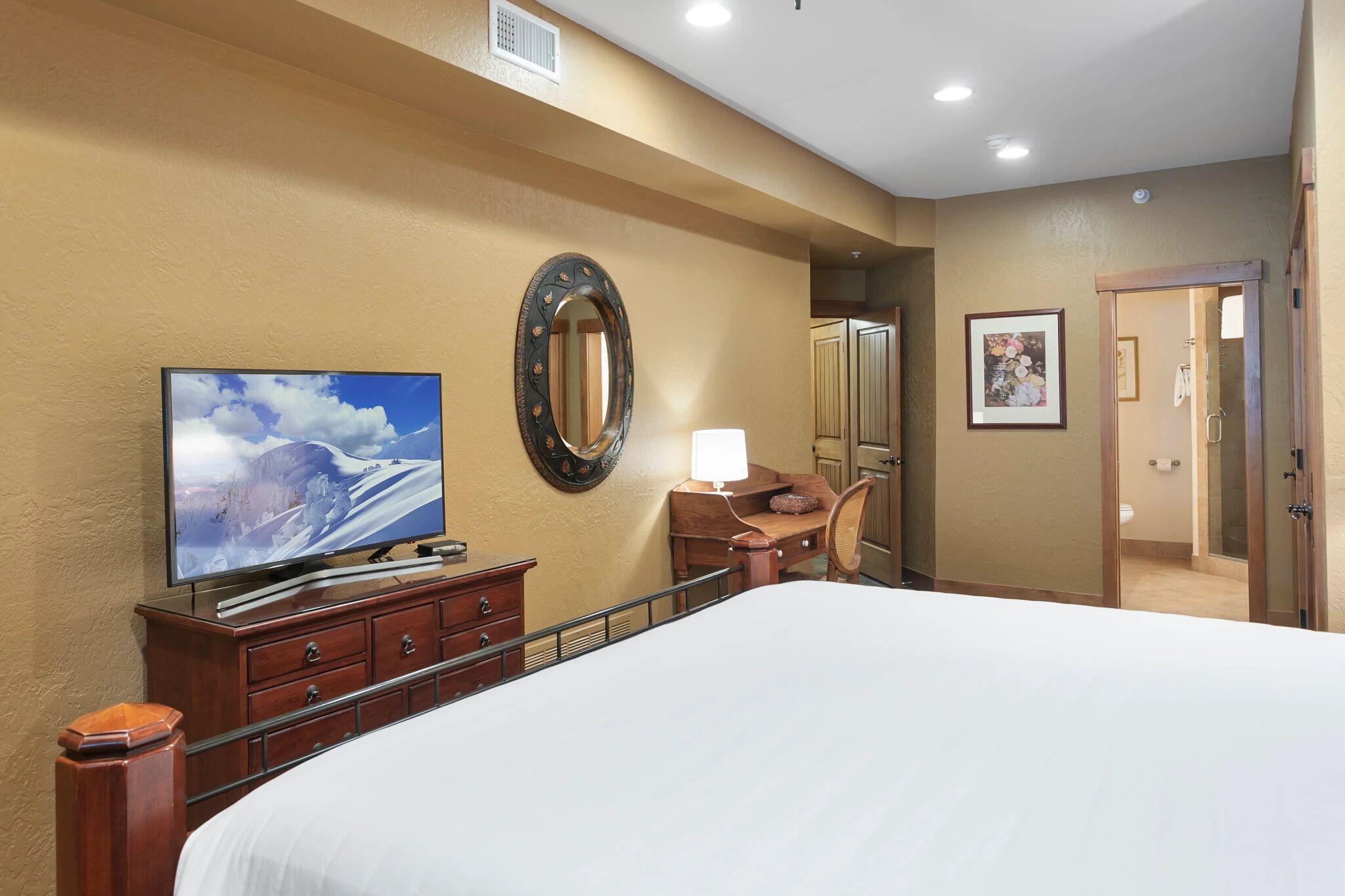 Une chambre d’hôtel avec un grand lit, un téléviseur posé sur une commode en bois, un miroir et une porte donnant sur une salle de bain.