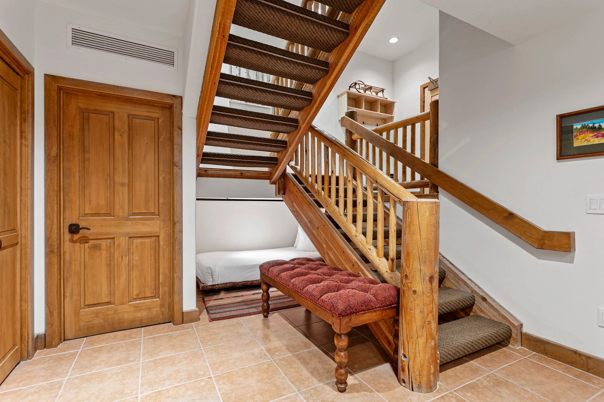 Una escalera de madera con un banco acolchado al pie, un sofá blanco y una puerta a la izquierda.