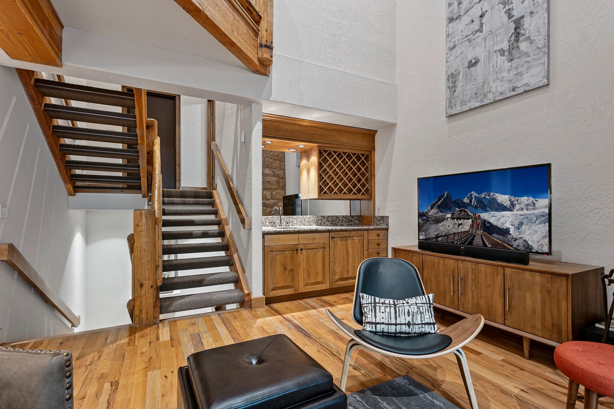 Een modern interieur met een houten trap, een keukenhoek en een flatscreen televisie waarop een berglandschap te zien is.
