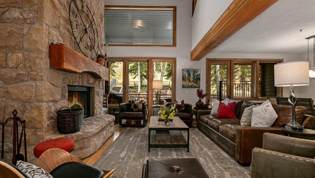 A spacious living room with a stone fireplace, wooden beams, large windows, and comfortable seating. - Sterling Lodge at Deer Valley Resort - Three Bedroom Condo with Hot Tub #111 3 Condo (Park City)