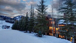 A lodge with a ski lift in the background, surrounded by snow-covered ground and tall evergreen trees. - Sterling Lodge at Deer Valley Resort - Three Bedroom Condo with Hot Tub #111 3 Condo (Park City)