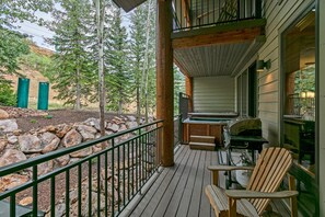 A wooden deck with a hot tub, a grill, and a chair.