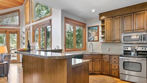 A modern kitchen with wooden cabinets, a large island, stainless steel appliances, and large windows.