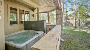 A hot tub under a covered patio with stone walls and a view of a wooded area.