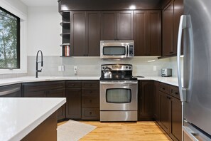 A modern kitchen with stainless steel appliances, dark wooden cabinets, and a white countertop. - Twin Pines at Deer Valley Resort - Three Bedroom Condo with Hot Tub #5 3 Condo (Park City)