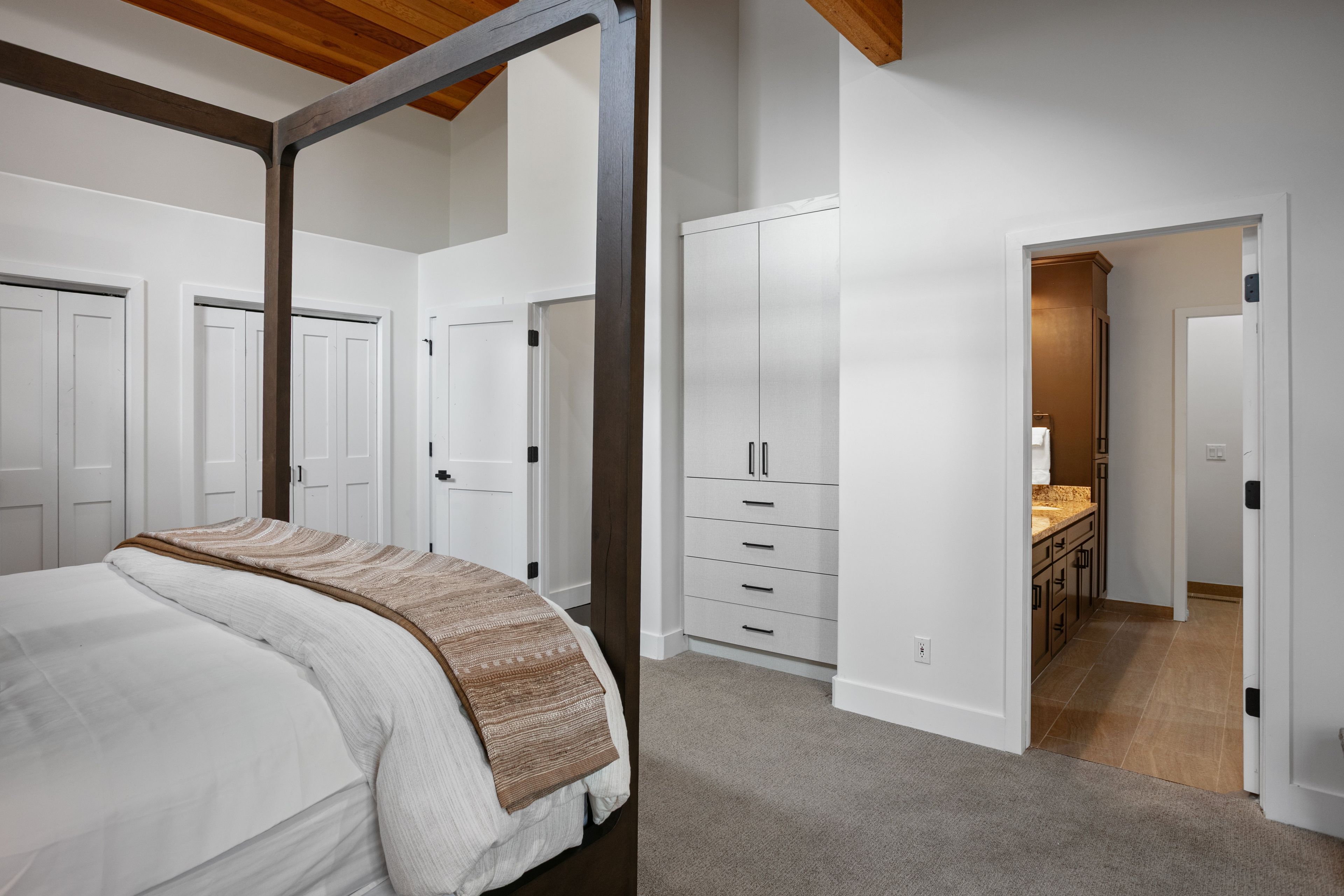 A bedroom with a four-poster bed, a walk-in closet, and a hallway leading to a bathroom.