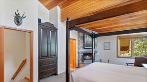 A bedroom with a large bed, wooden ceiling beams, a stone fireplace, and a wardrobe.