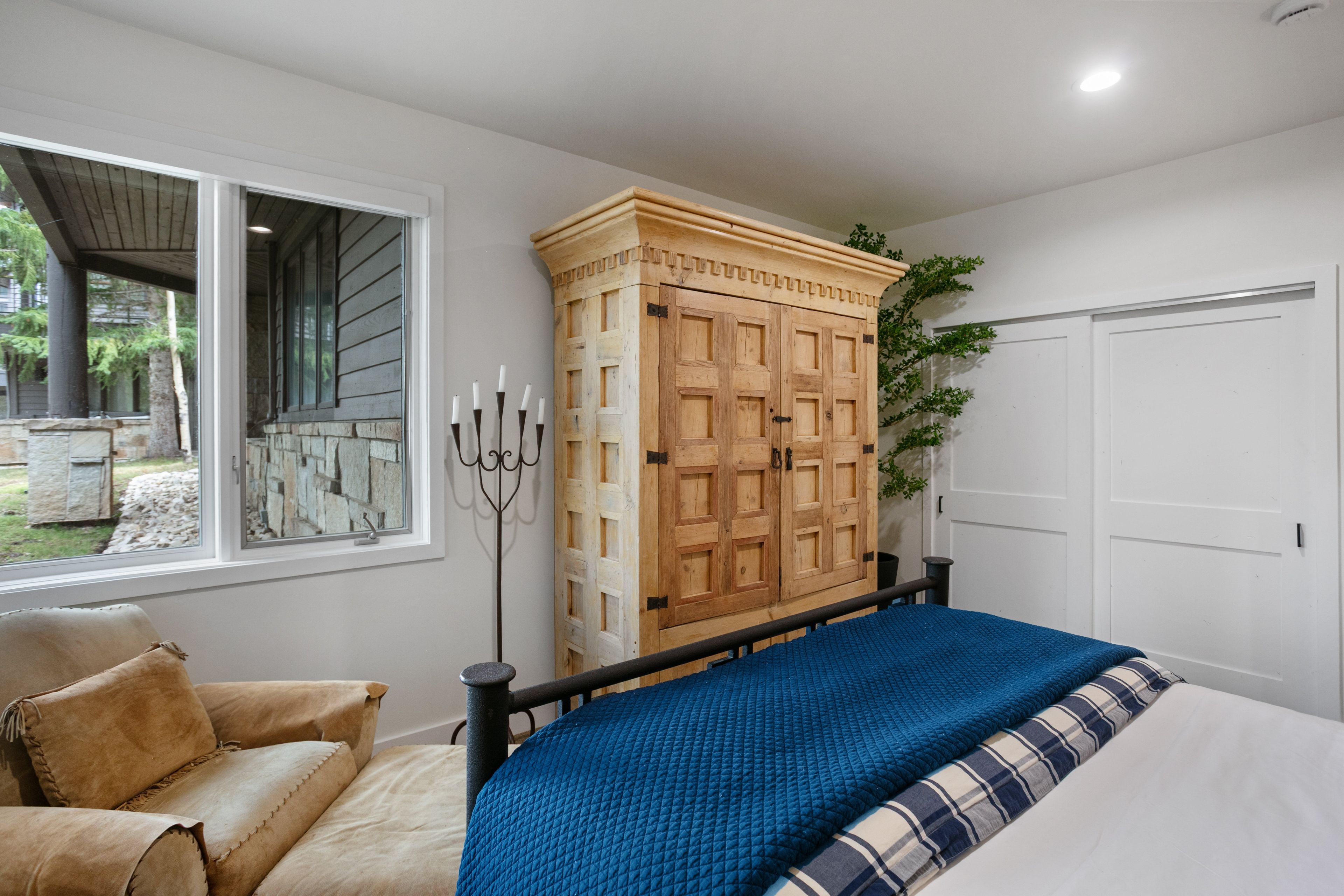 A bedroom with a bed, a wooden wardrobe, a window, and a door.