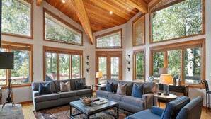 A spacious living room with large windows, a wooden ceiling, and a modern sofa set.