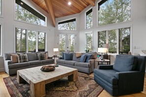 A spacious living room with a high ceiling, large windows, and a mix of sofas and chairs.