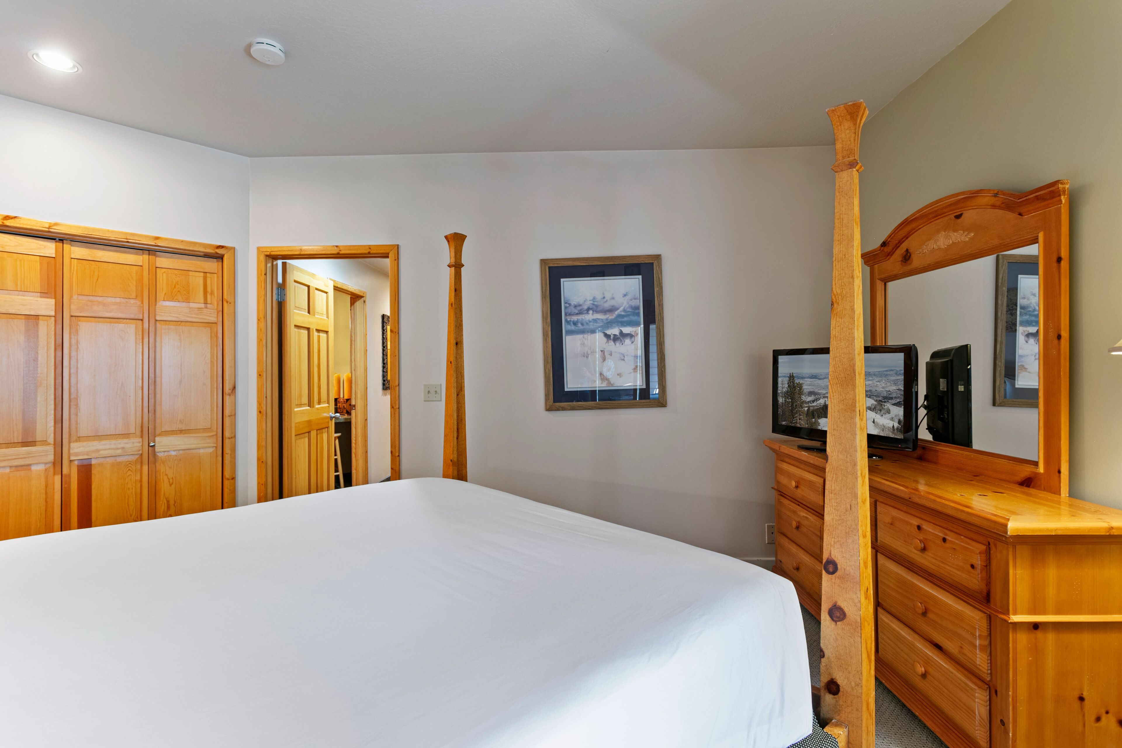 A bedroom with a large bed, wooden wardrobe, and a dresser with a mirror.
