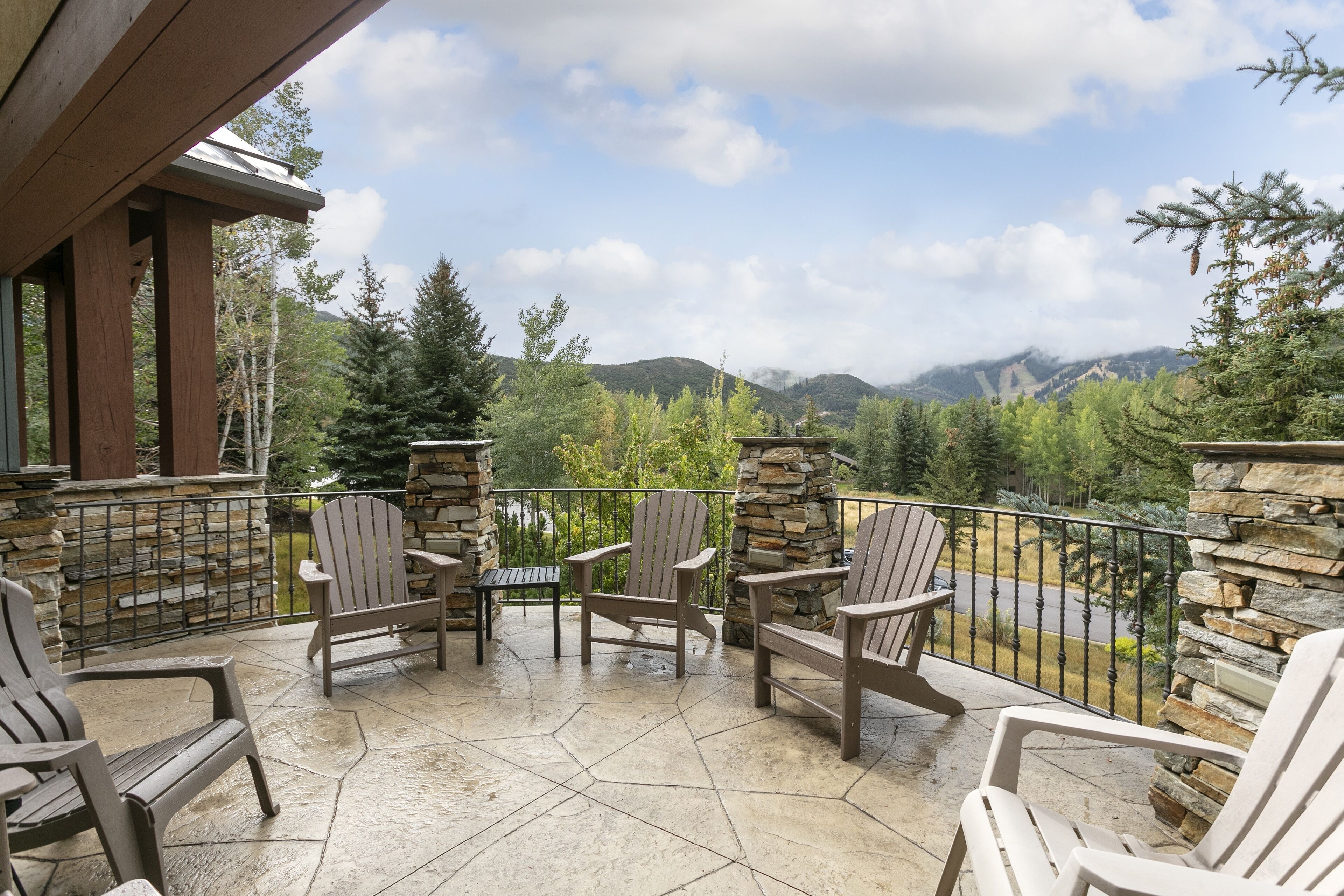 Une terrasse couverte, dotée de chaises Adirondack et d’un mur en pierre, qui offre une vue sur un paysage montagneux.