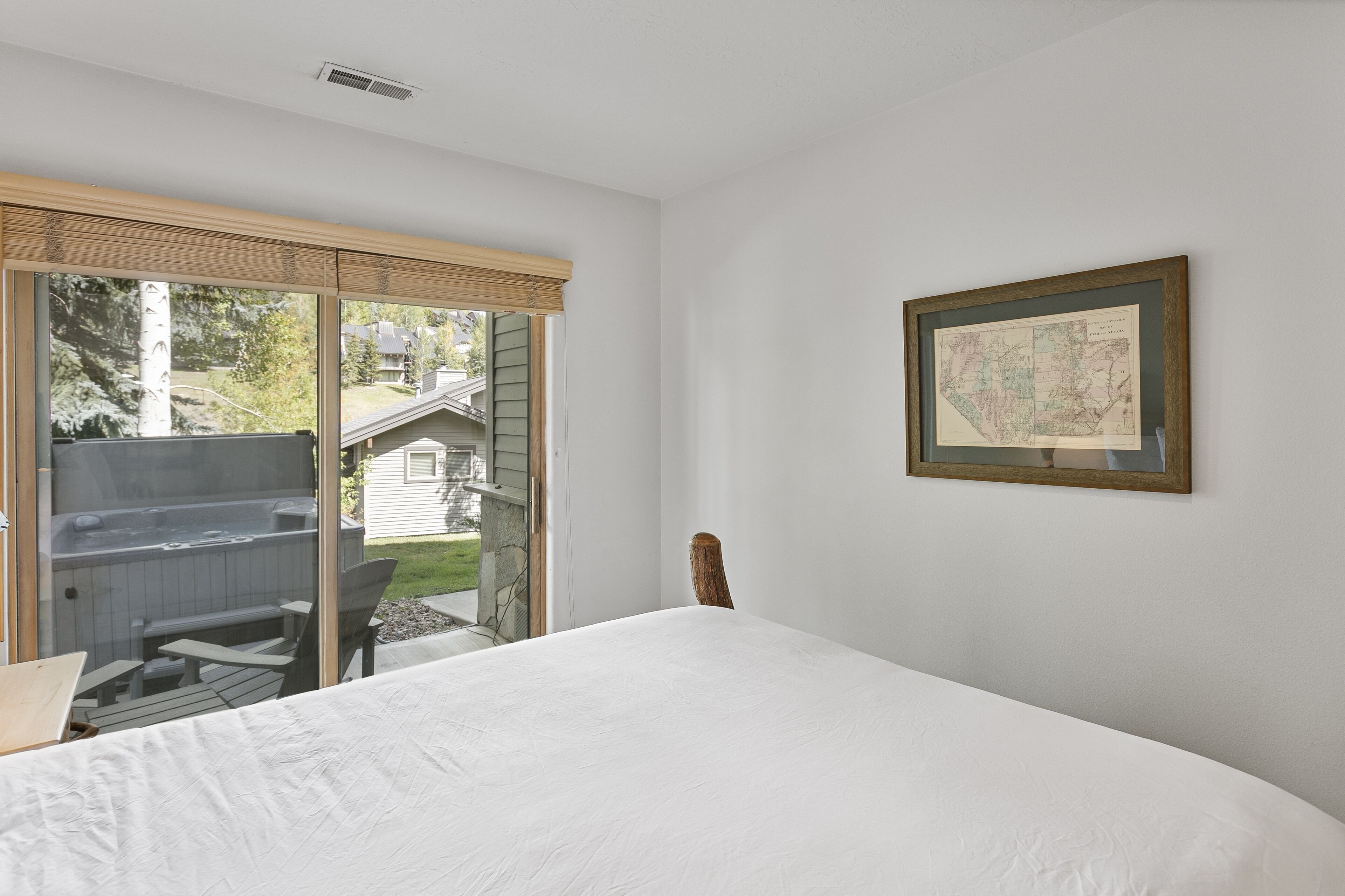 A bedroom with a large bed, a wooden chair, a hot tub, and a sliding glass door leading to a backyard.