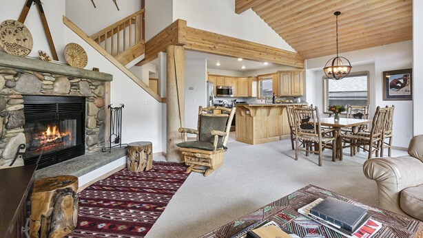 A spacious living area with a stone fireplace, wooden ceiling beams, and a dining area with wooden chairs and a table. - Boulder Creek at Deer Valley Resort - Three Bedroom Condo with Hot Tub #1119 3 Condo (Park City)