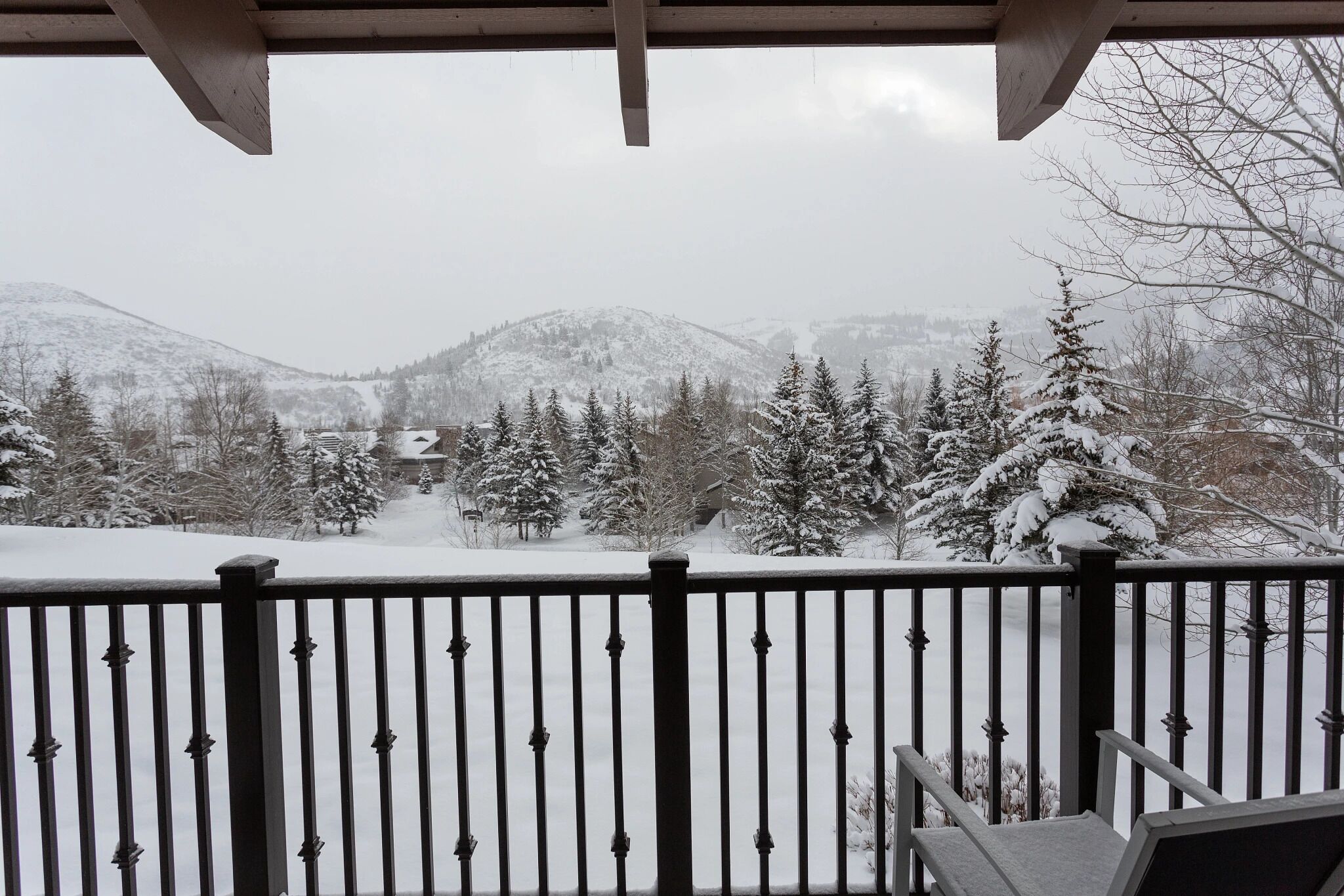A snow-covered landscape with a view of mountains and trees from a balcony with a metal railing.