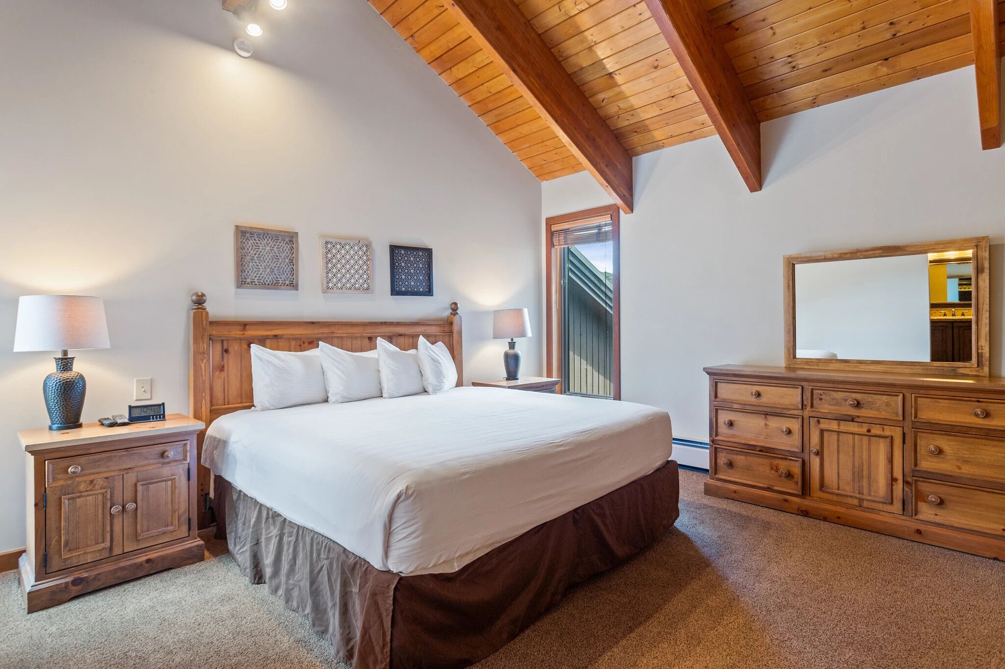 A bedroom with a large bed, wooden headboard, two bedside tables with lamps, a dresser, and a mirror.