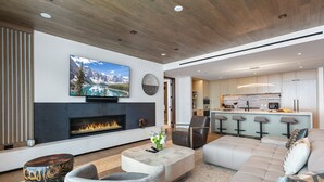 A modern living room with a fireplace, a large TV, and a kitchen area with bar stools. - Argent at Deer Valley Resort - Three Bedroom Deluxe #405 3 Condo (Park City)