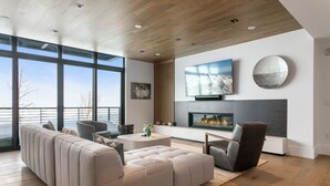 A modern living room with a large sectional sofa, a fireplace, a flat-screen TV, and a large window overlooking a cityscape. - Argent at Deer Valley Resort - Three Bedroom Deluxe #405 3 Condo (Park City)