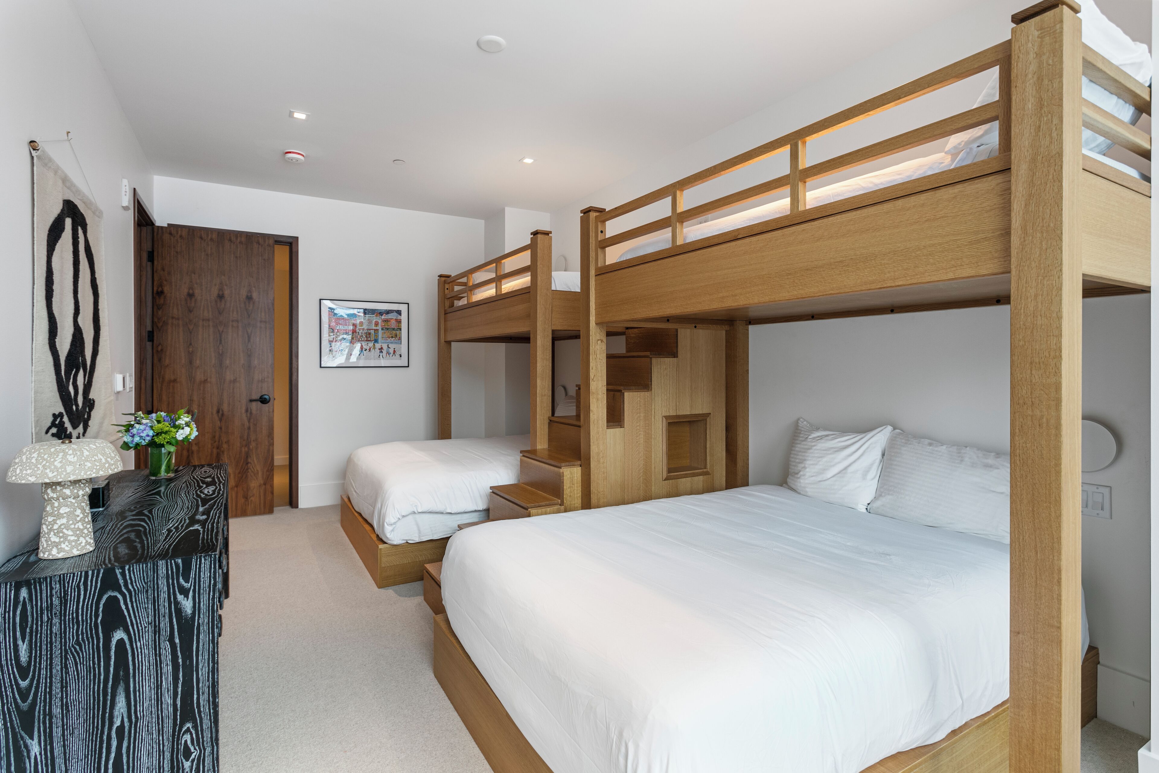 A room with bunk beds, a wooden desk, and a framed picture on the wall.