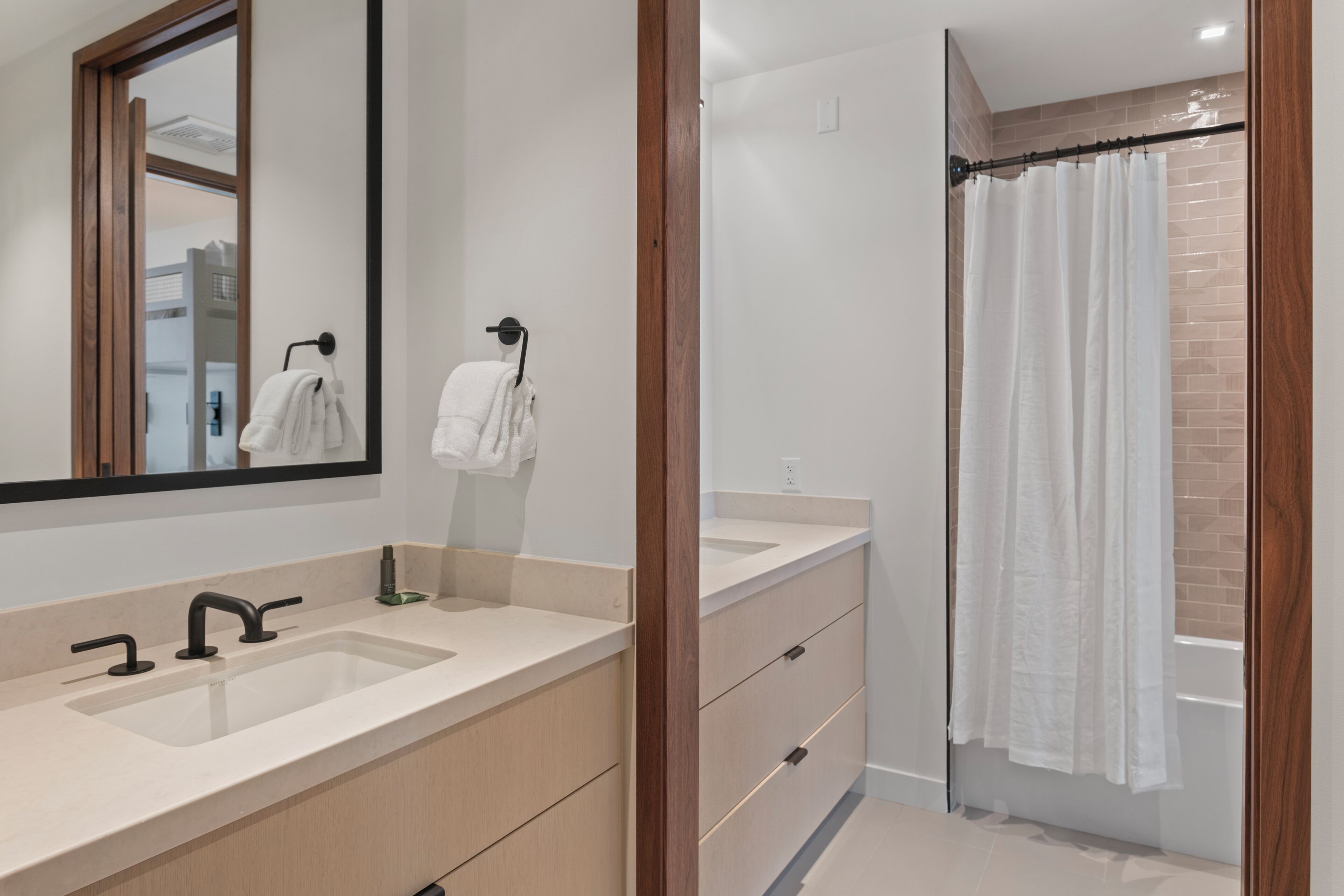 Un bagno moderno con uno specchio grande, due lavabi, una doccia con tenda e mobili in legno.