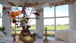 Une table ornée d’un vase de fleurs, d’un bol en laiton et d’un chandelier, placée près d’une fenêtre donnant sur un champ verdoyant.