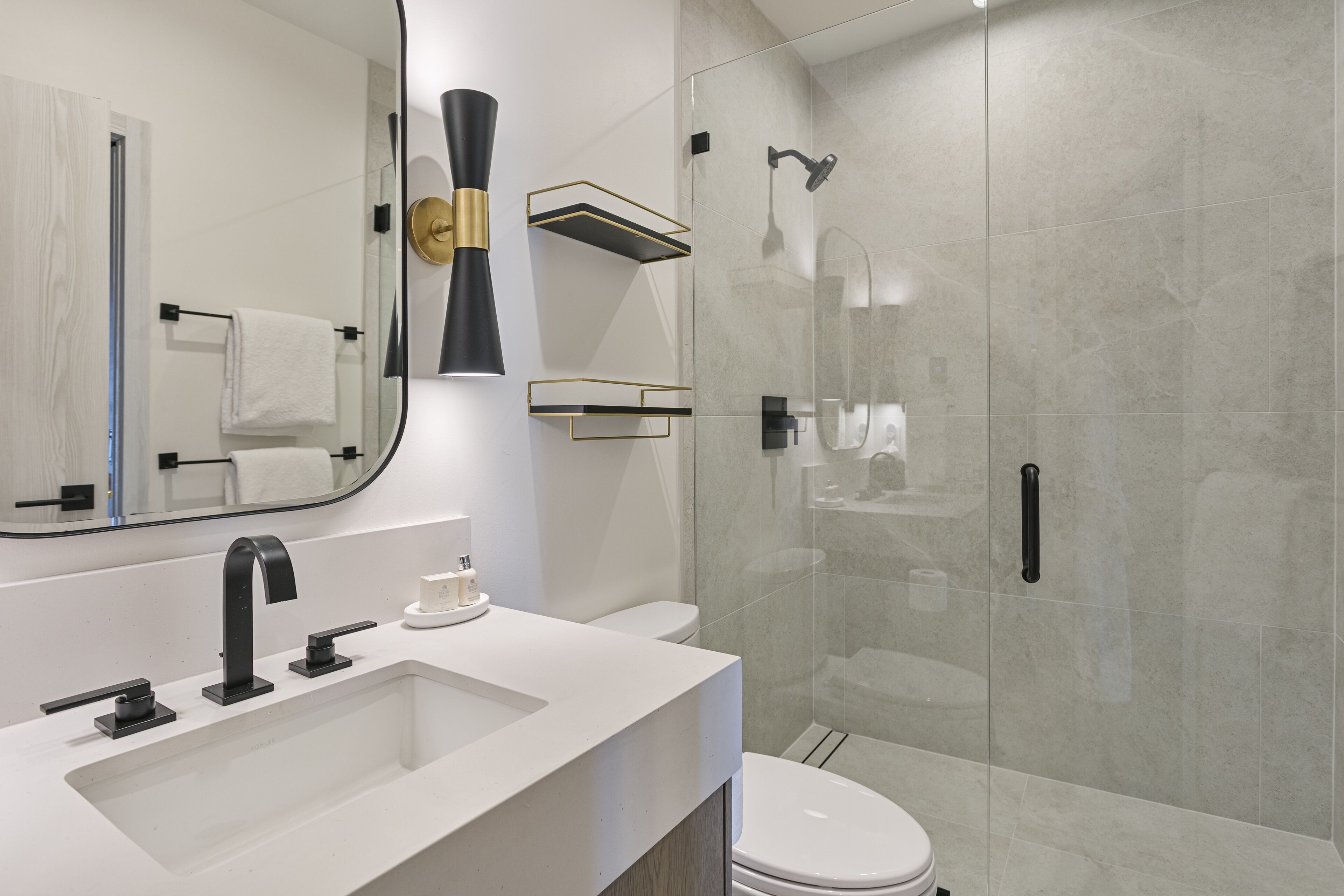 Un baño moderno con un lavabo blanco, un grifo negro y una zona de ducha con mampara de vidrio.