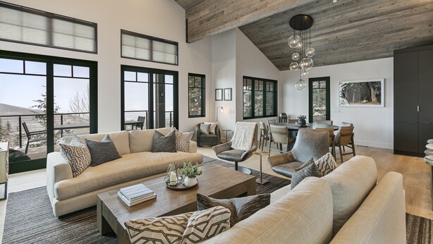 A spacious living room with a high ceiling, large windows, and a modern chandelier.