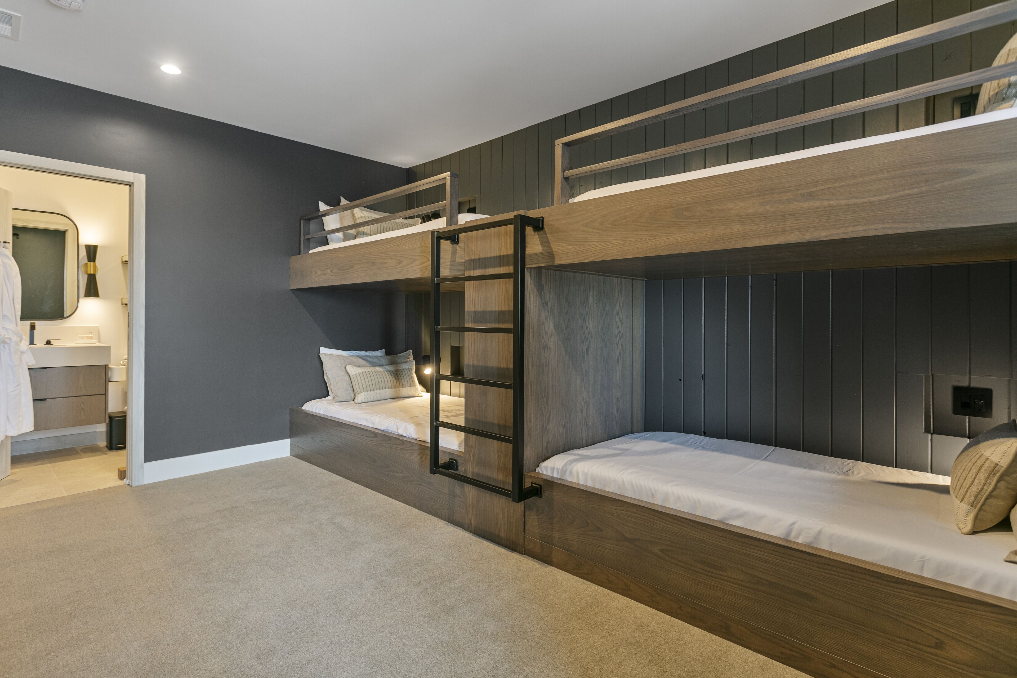 Habitación con literas, una escalera de madera, un escritorio pequeño y un espejo.
