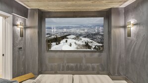 A room with a large window offering a snowy mountain view, a wooden ceiling, and two wall-mounted light fixtures.