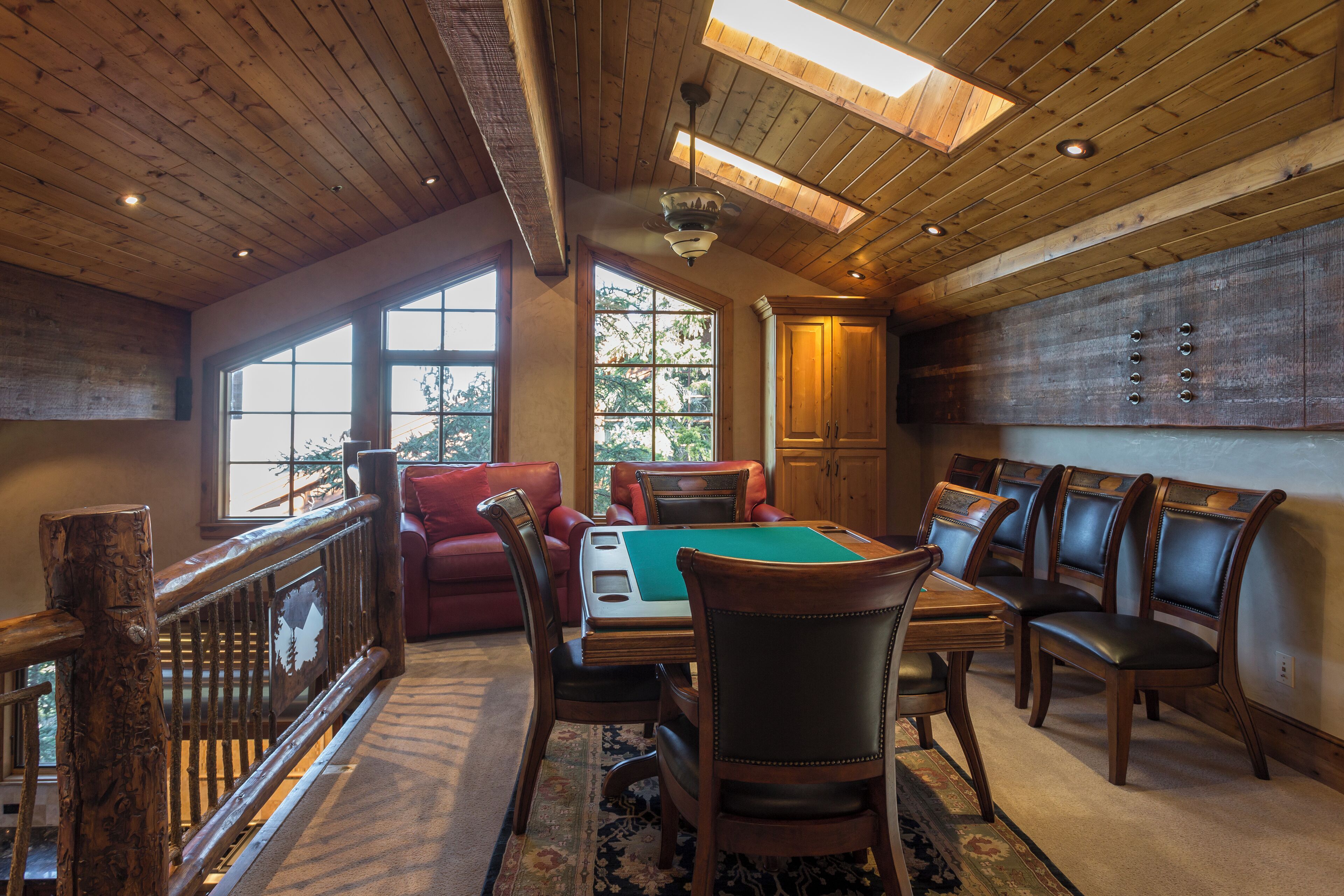 A wooden interior with a pool table, leather chairs, and a balcony.